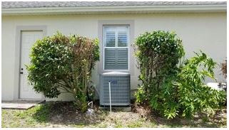 AC unit on the side of home positioned between two shrubs under the window.