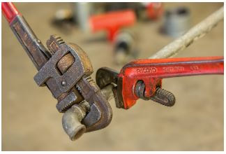 Using two wrenches on pipe; one to grip pipe and the other to twist or turn the 90 degree elbow at the end of the pipe.